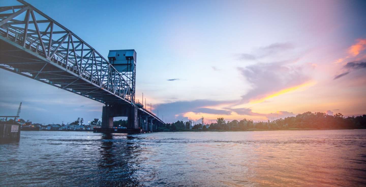 The Wilmington bridge stretches over water toward the skyline at sunset.