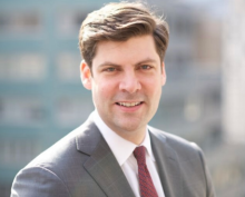 Devin in a gray suit jacket, white shirt and red tie