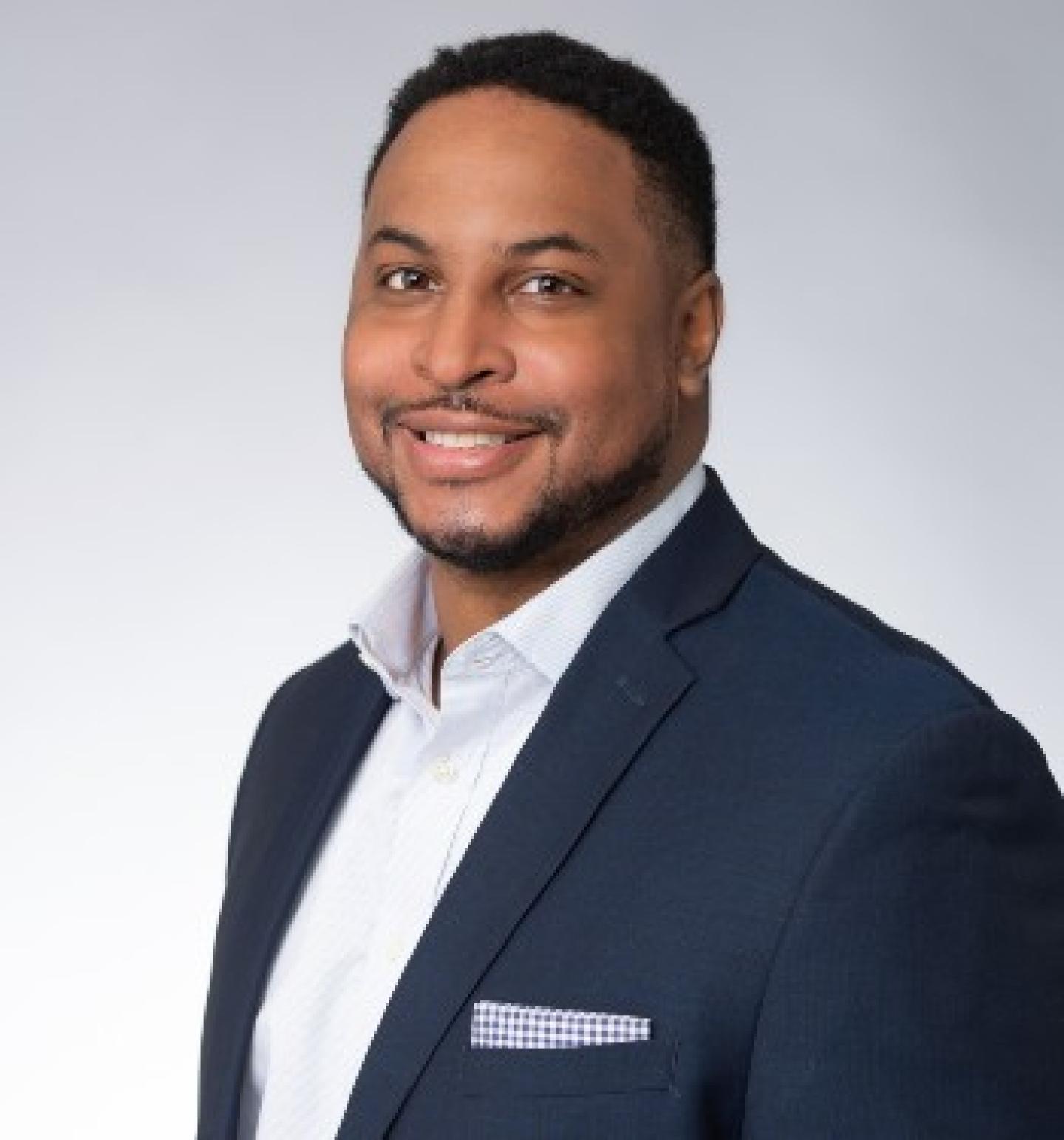 Panelist, Rich Grant is smiling. He's wearing a navy blue blazer and white collar shirt.